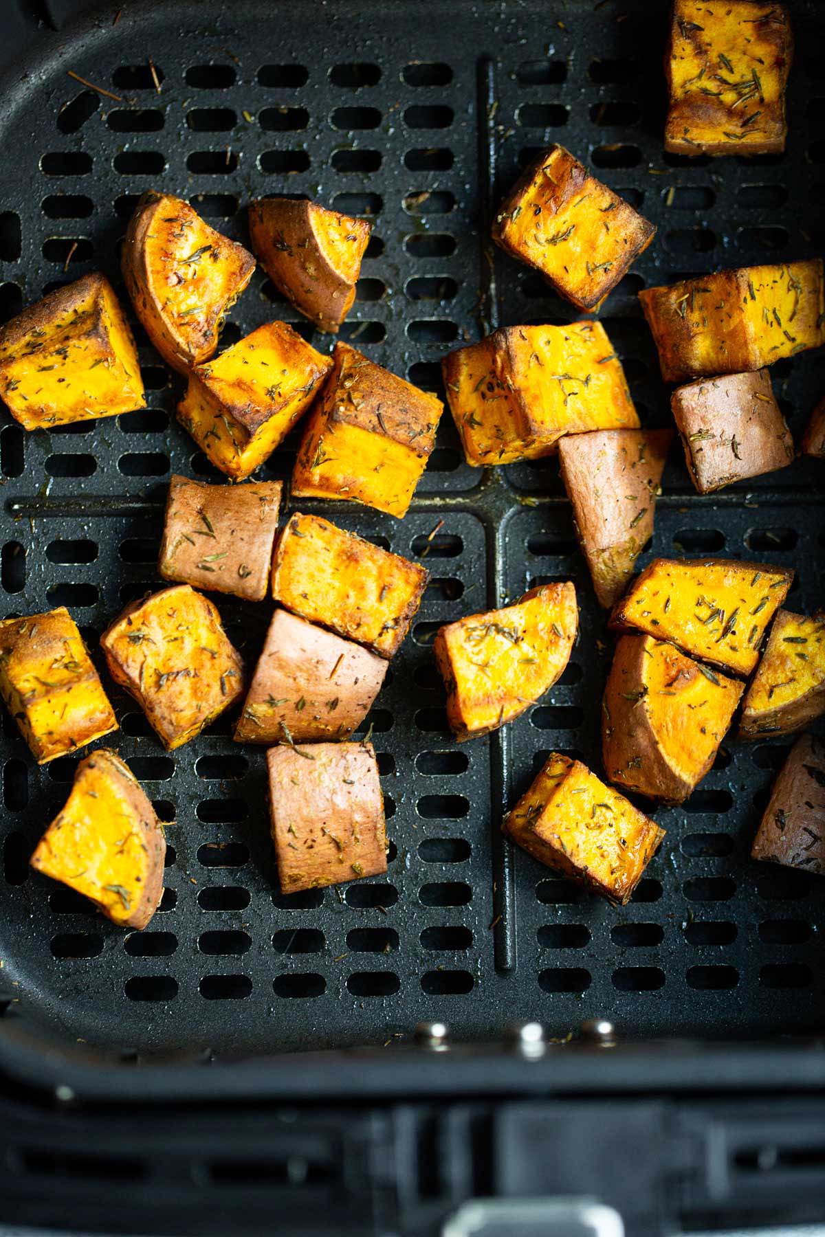 Cooked sweet potato cubes in air fryer basket.