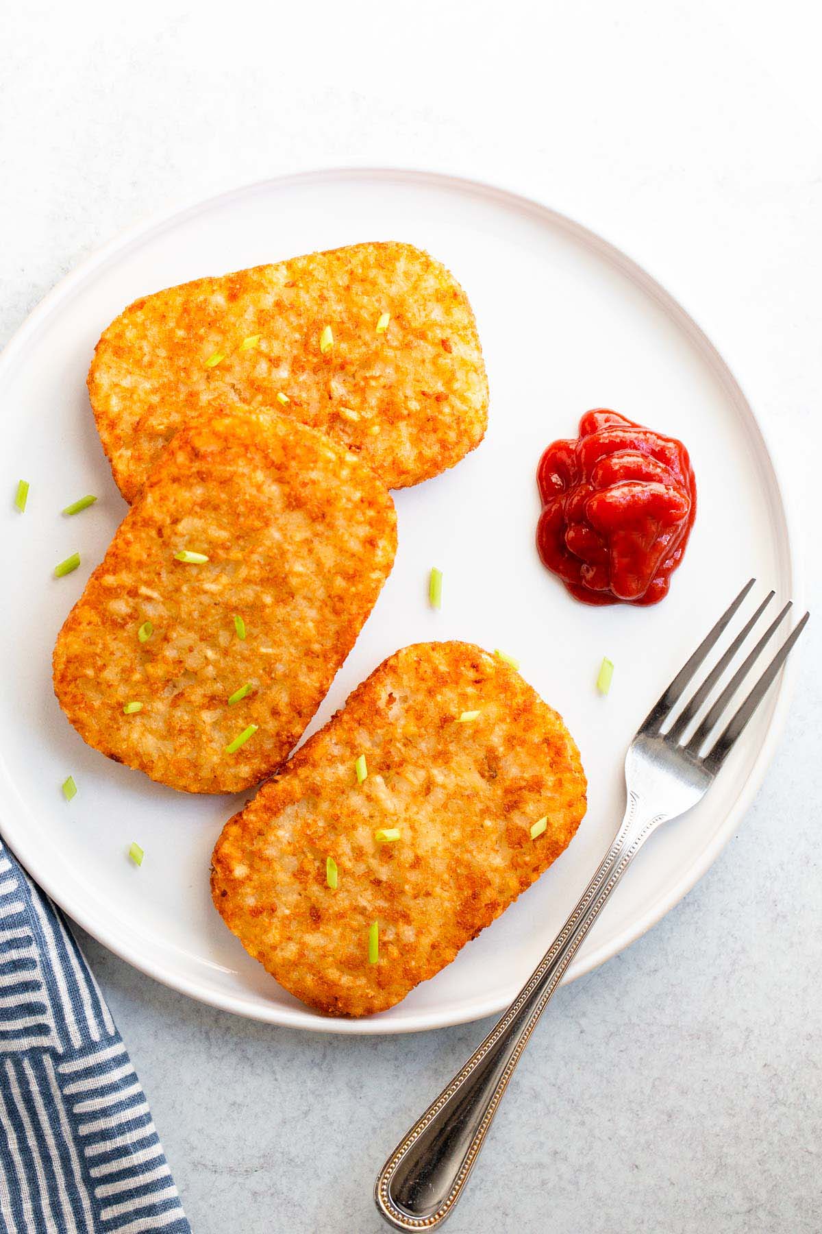 Hash brown patties with ketchup on a white plate.