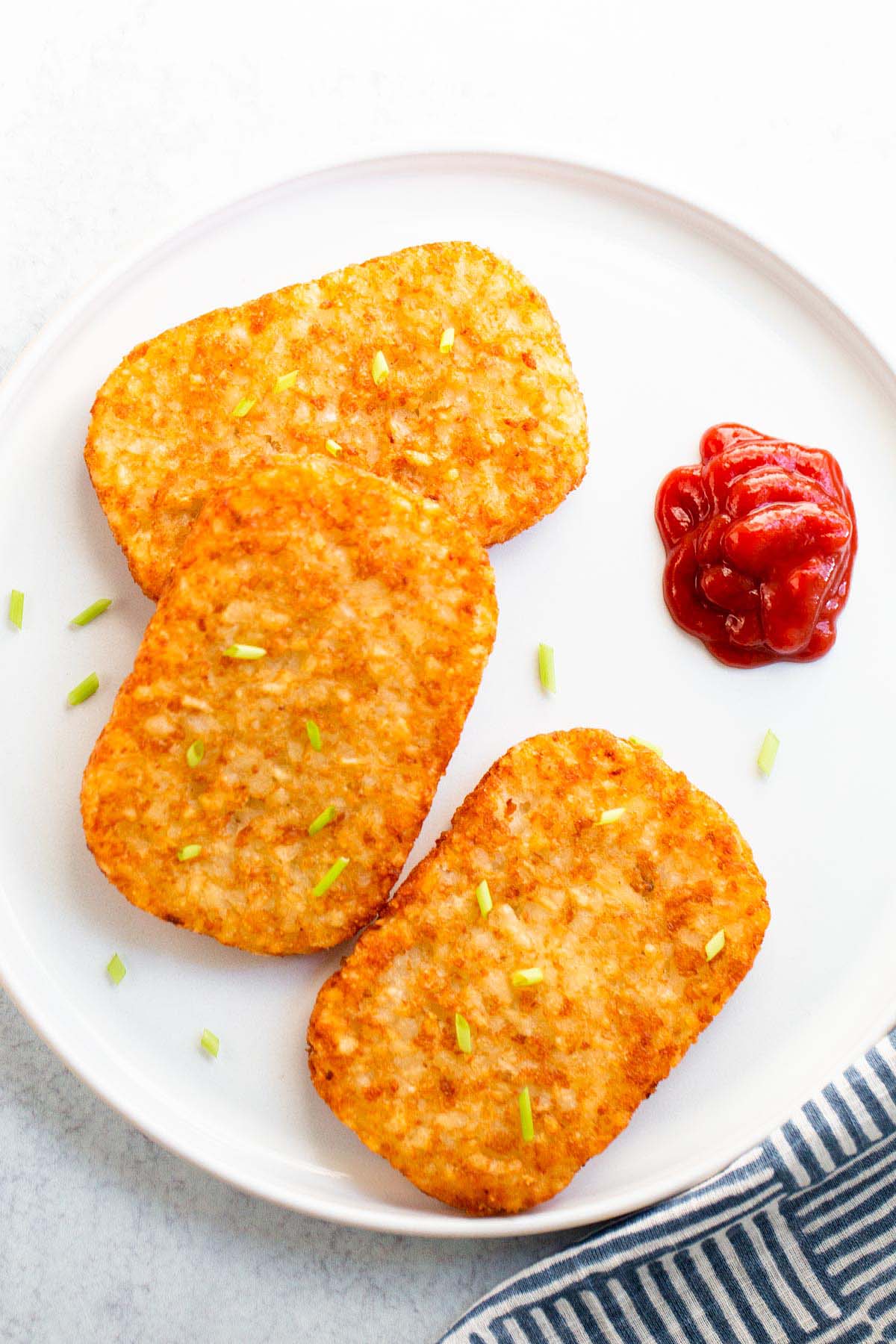 Hash brown patties with ketchup on a white plate.