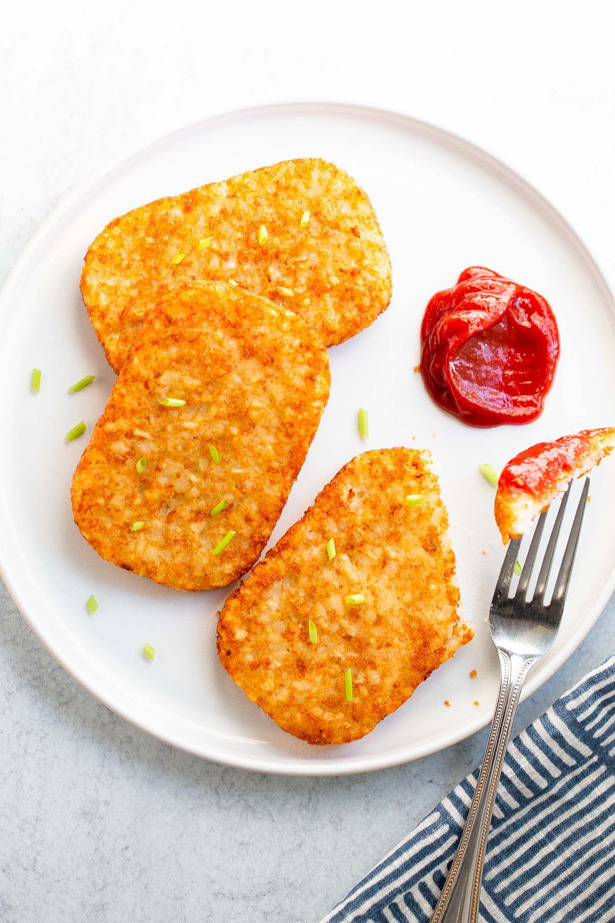 Hash brown patties with ketchup on a white plate.