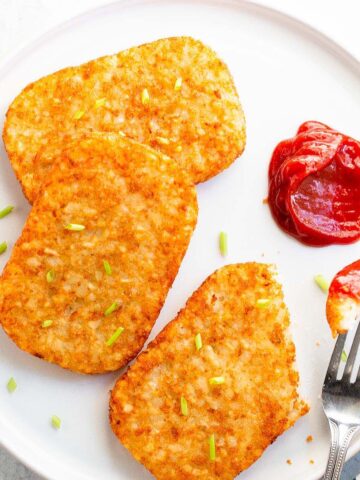 Hash brown patties with ketchup on a white plate.