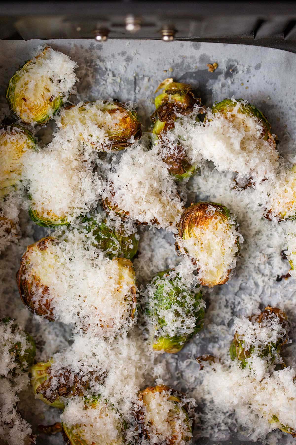 Brussels sprouts topped with grated parmesan in air fryer basket.