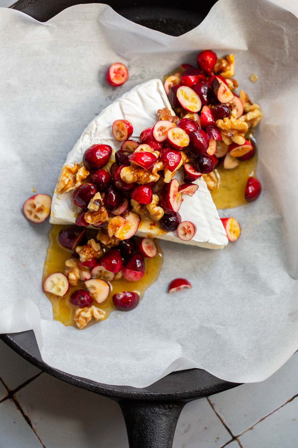 Uncooked brie wedge topped with cranberries and walnuts.