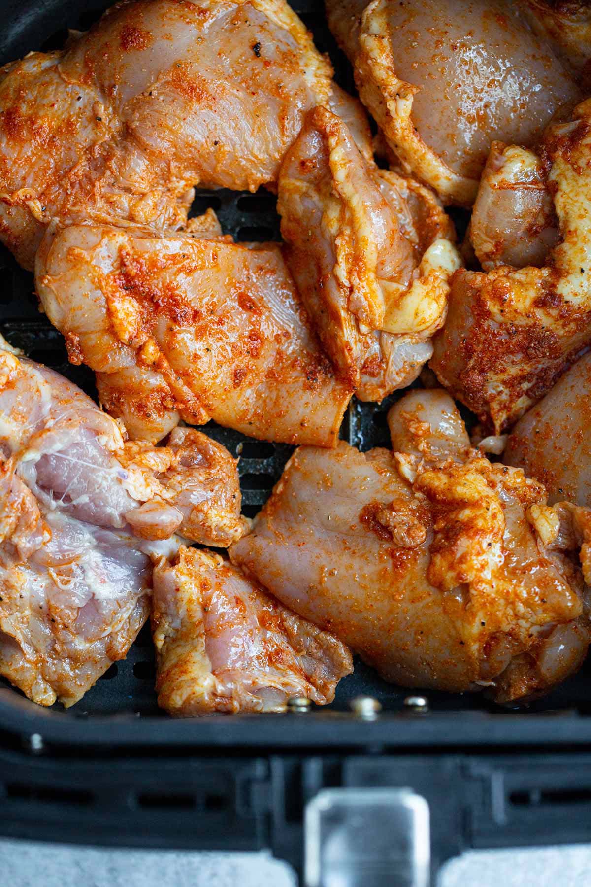 Uncooked chicken thighs in air fryer basket.