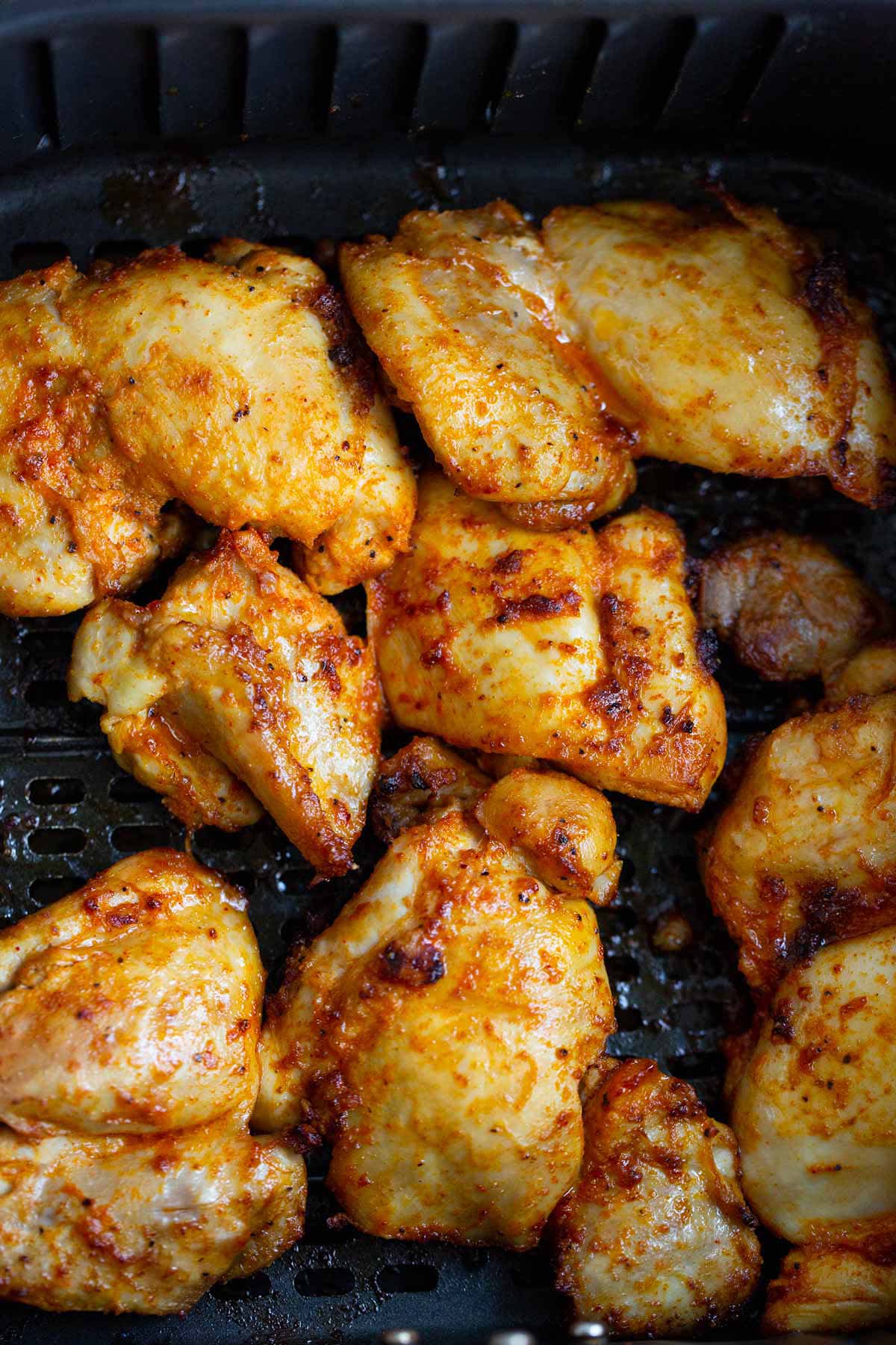 Cooked chicken thighs in air fryer basket.