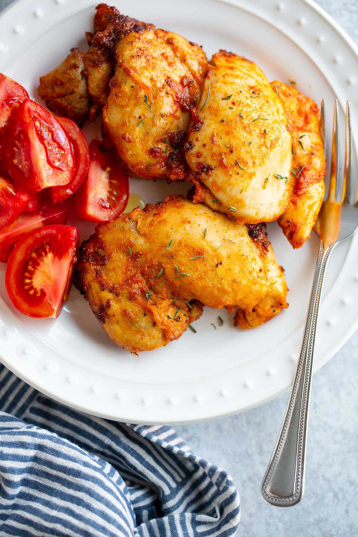 Chicken thighs on a plate with tomatoes on the side.