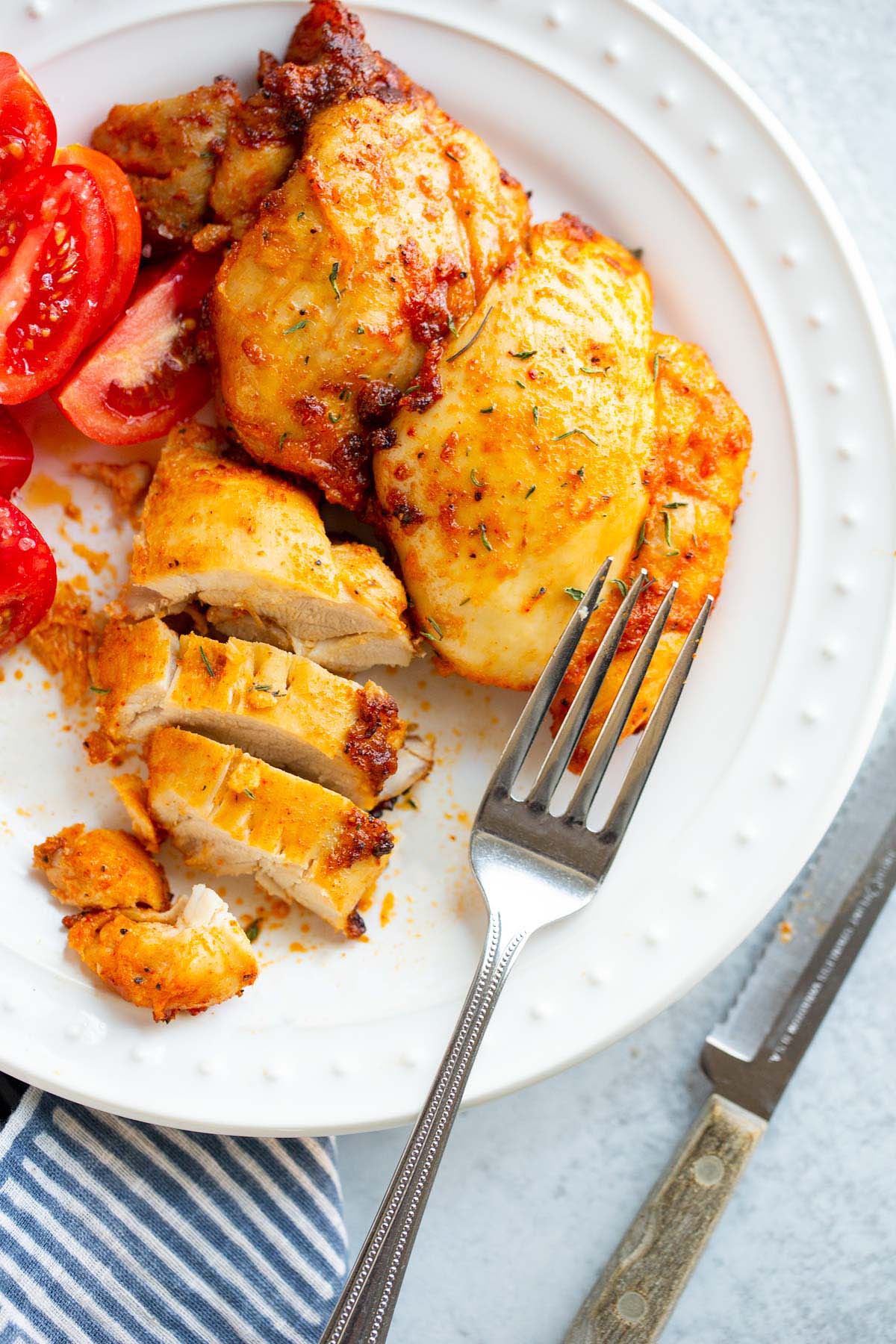 Sliced air fried chicken thigh on a plate with tomatoes on the side.