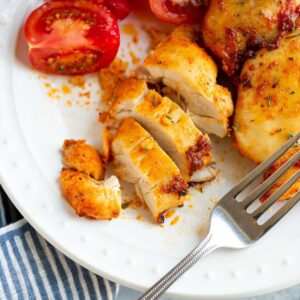 Sliced air fried chicken thigh on a plate with tomatoes on the side.