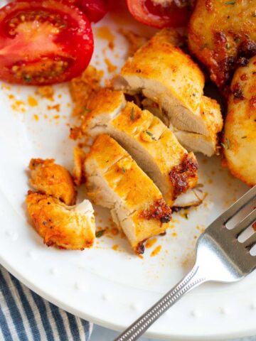 Sliced air fried chicken thigh on a plate with tomatoes on the side.