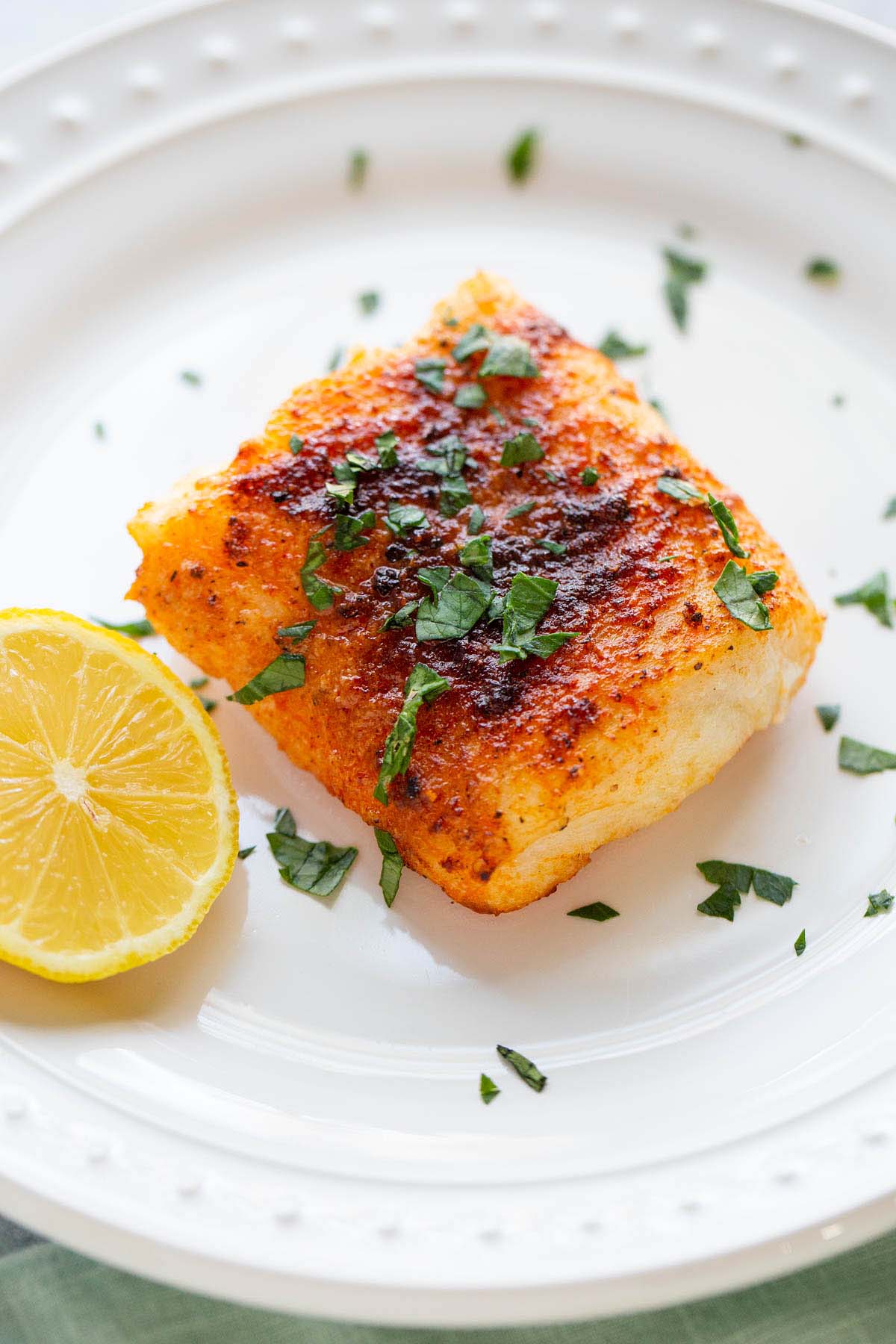 Air fryer cod on a plate with parsley on top and lemon on the side.