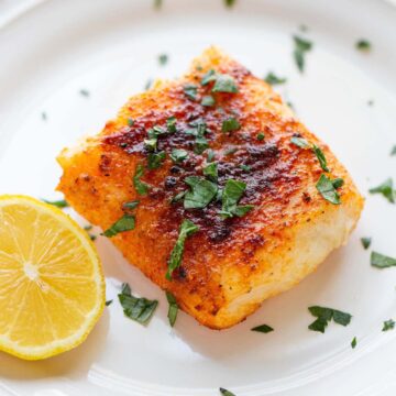 Air fryer cod on a plate with parsley on top and lemon on the side.