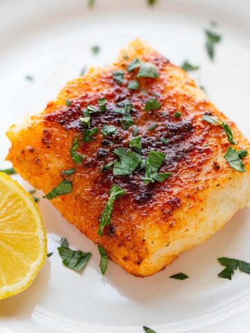 Air fryer cod on a plate with parsley on top and lemon on the side.