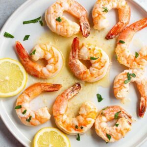 Garlic butter shrimp on a plate with lemons and fresh parsley.