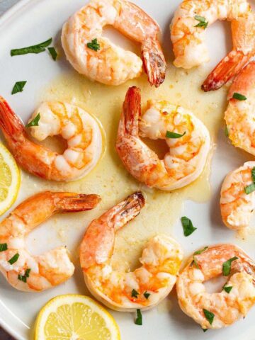 Garlic butter shrimp on a plate with lemons and fresh parsley.