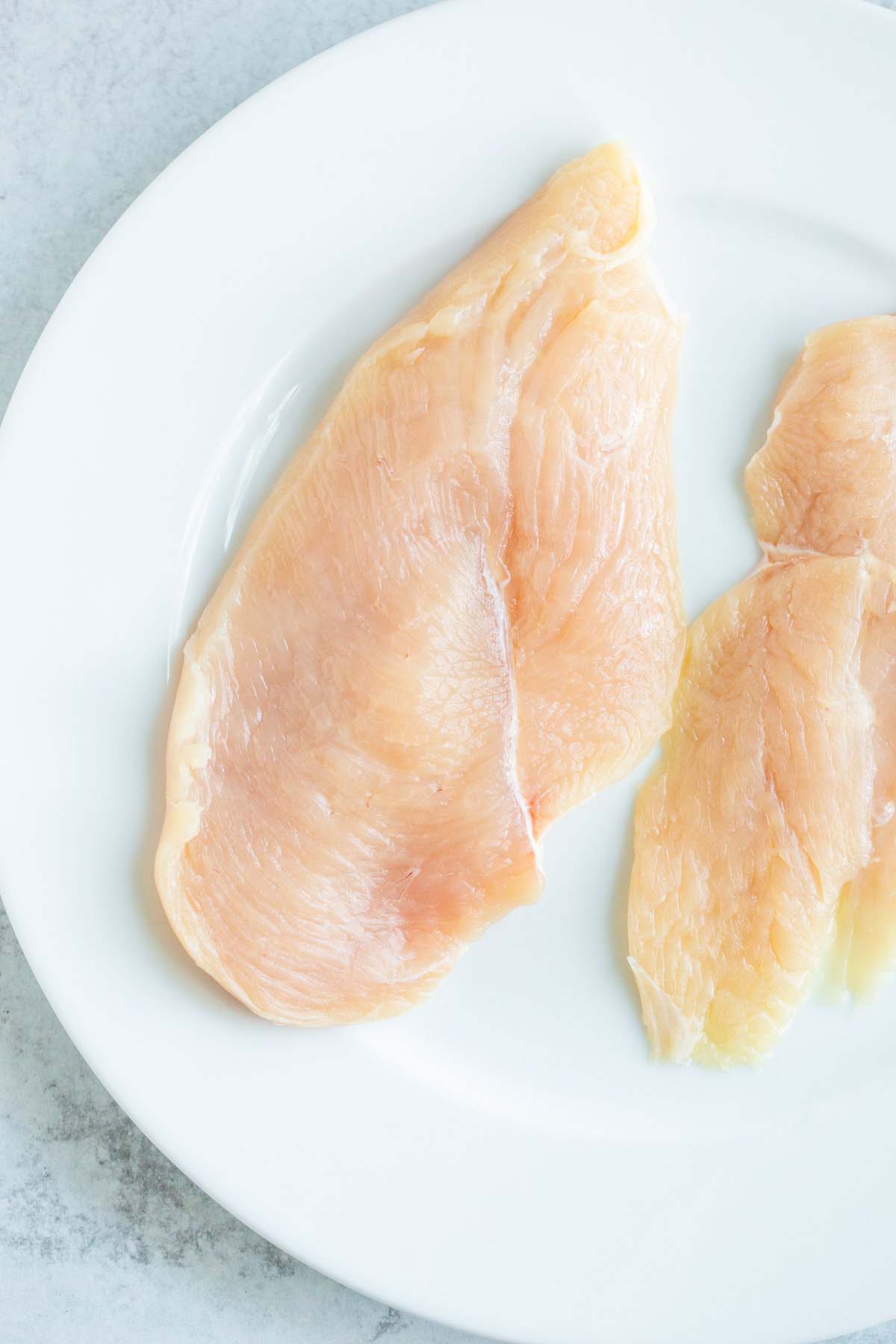 Raw chicken breasts on a plate.