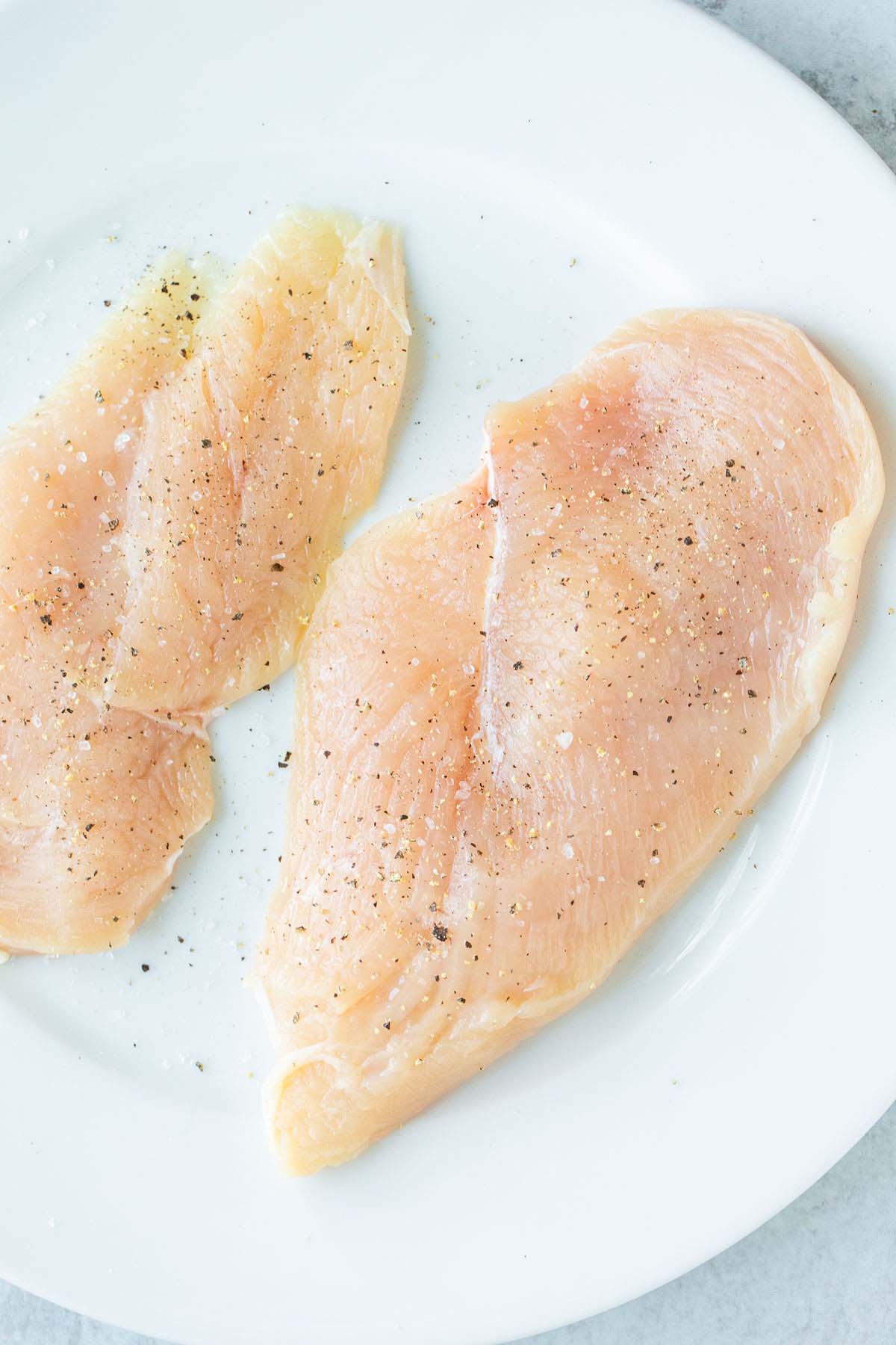 Raw chicken breast seasoned with salt and pepper.