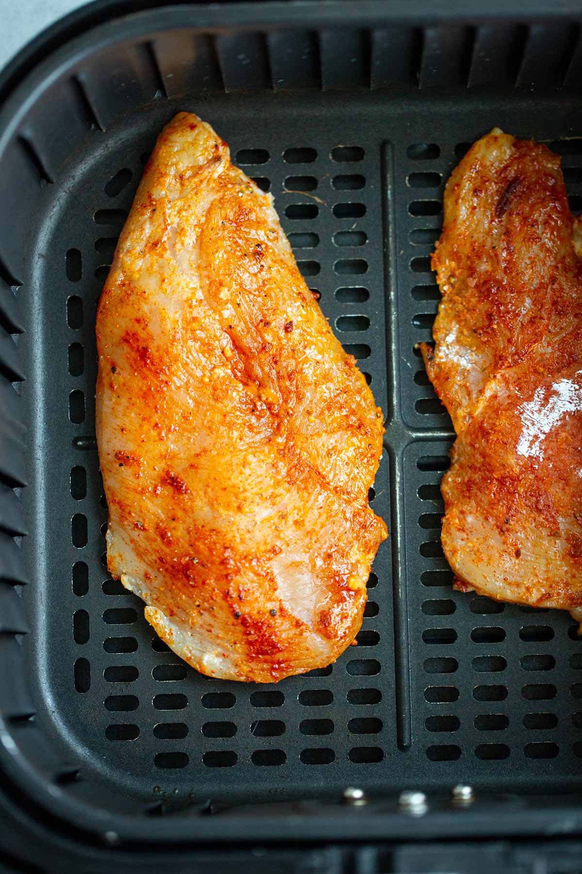 Raw chicken breasts in air fryer basket.