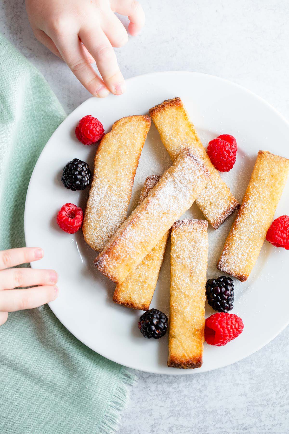 Kids hands reaching for air fried french toast sticks.