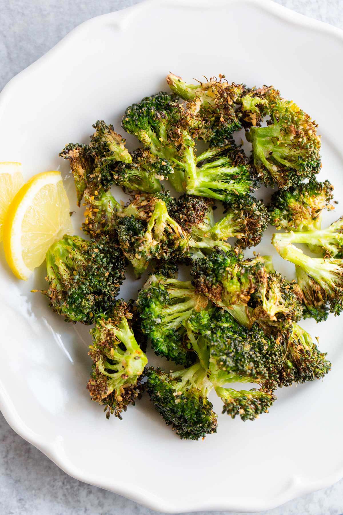 Air fried broccoli on a white plate with lemon slices.