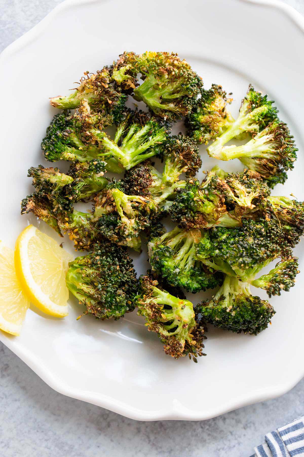 Air fried broccoli on a white plate with lemon slices.