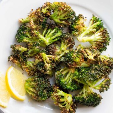 Air fried broccoli on a white plate with lemon slices.