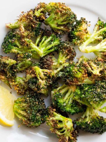 Air fried broccoli on a white plate with lemon slices.