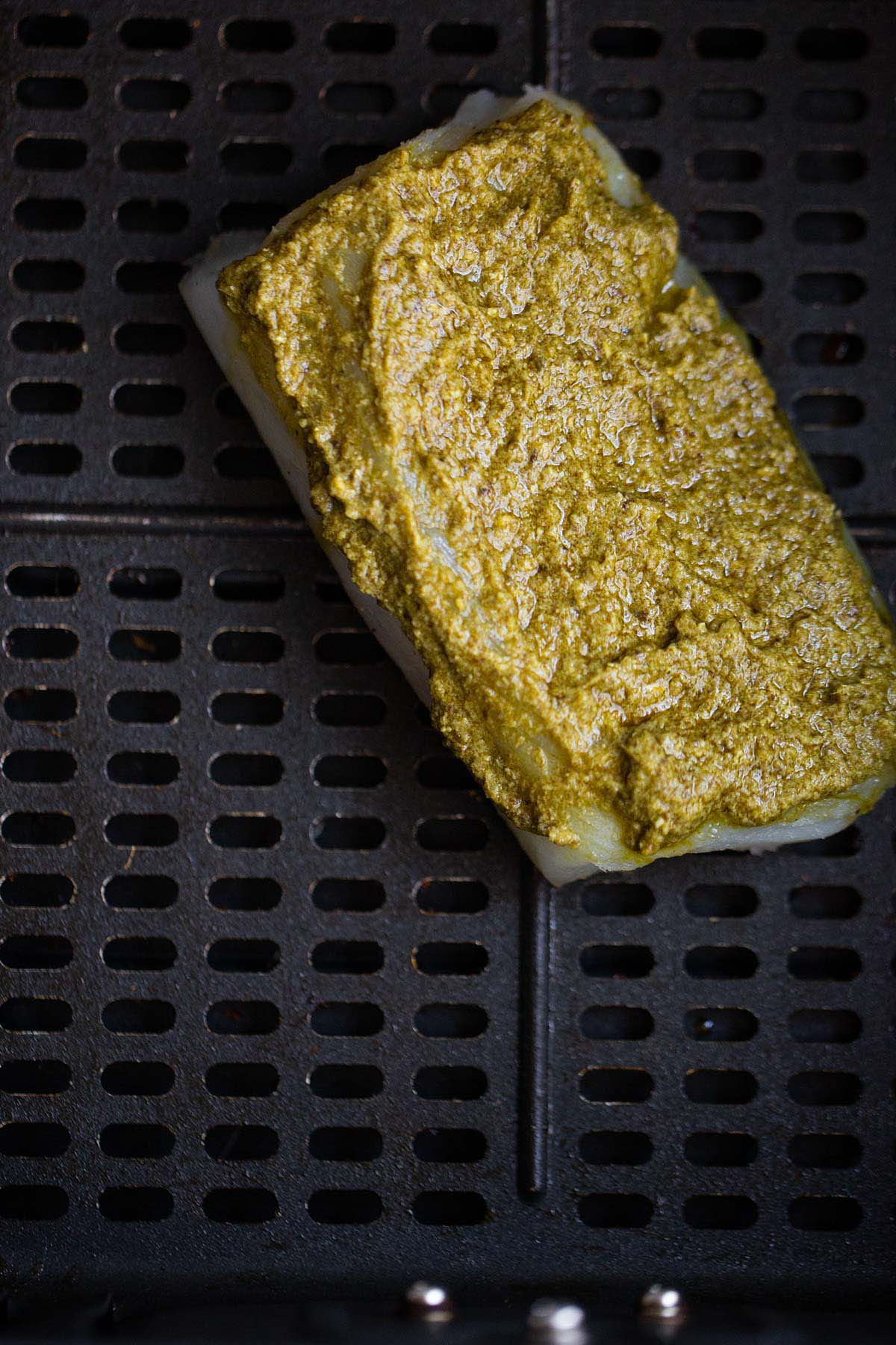 Uncooked pesto cod in air fryer basket.