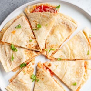 Air fryer pizza quesadilla on a white plate topped with chopped basil leaves.