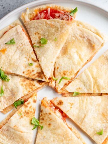 Air fryer pizza quesadilla on a white plate topped with chopped basil leaves.