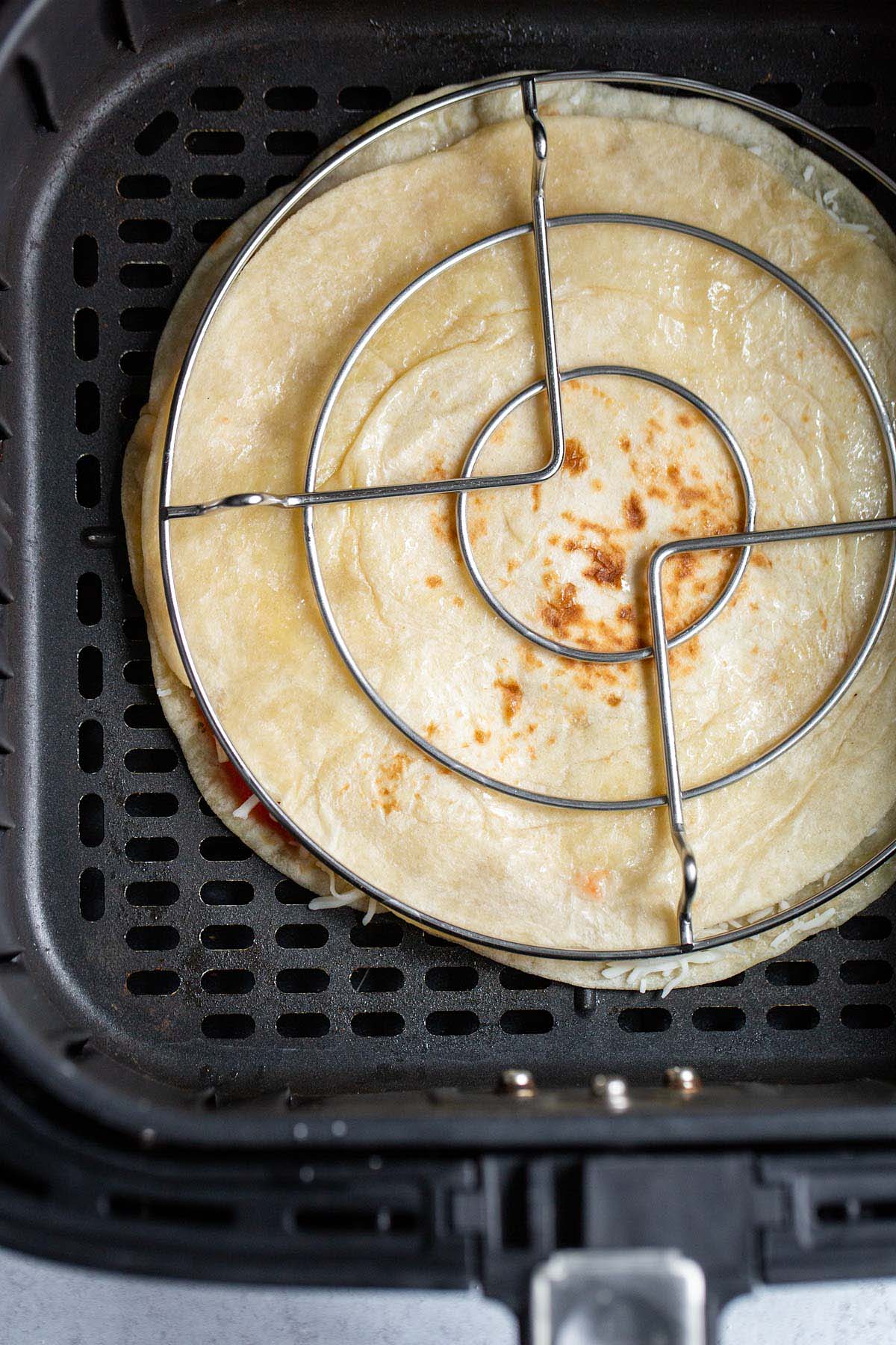 Pizza quesadilla in air fryer with trivet on top.