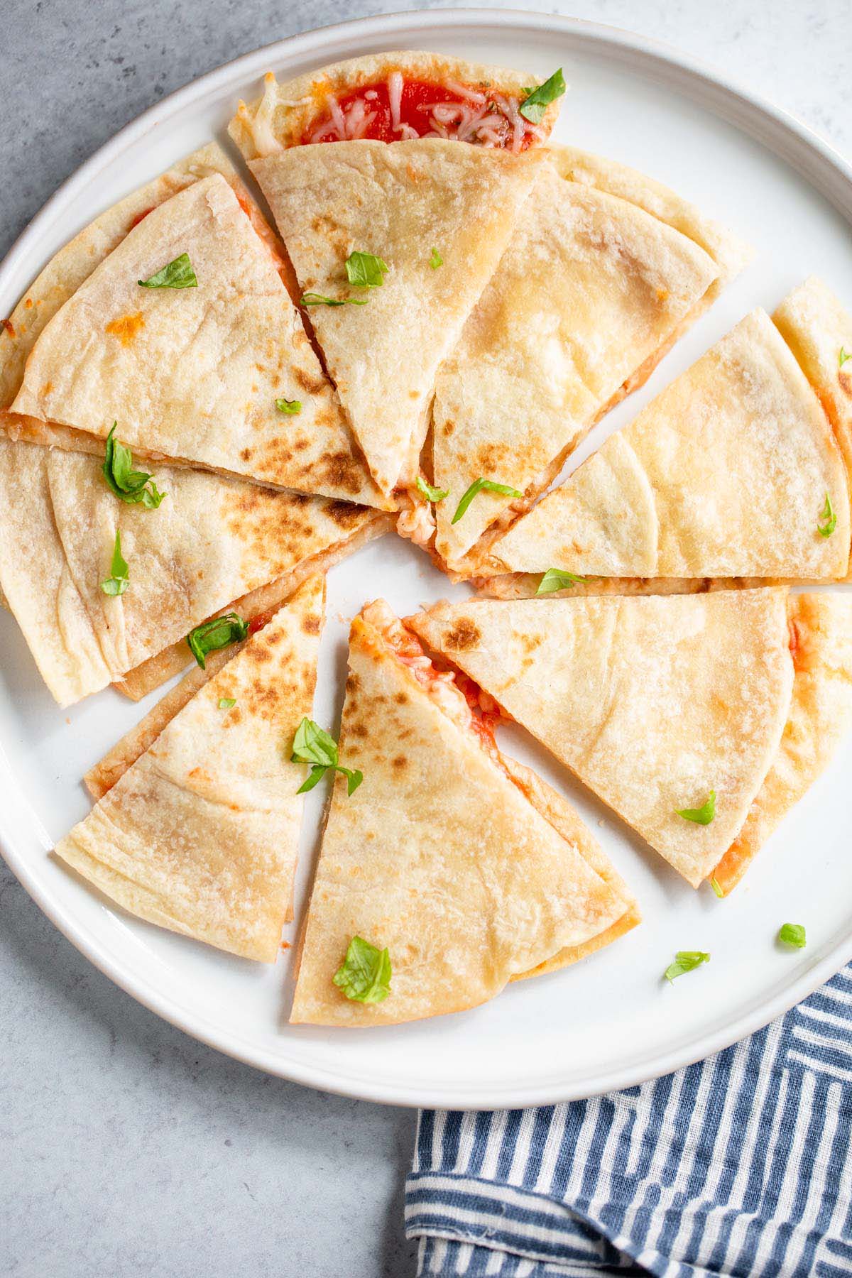 Air fryer pizza quesadilla on a white plate topped with chopped basil leaves.