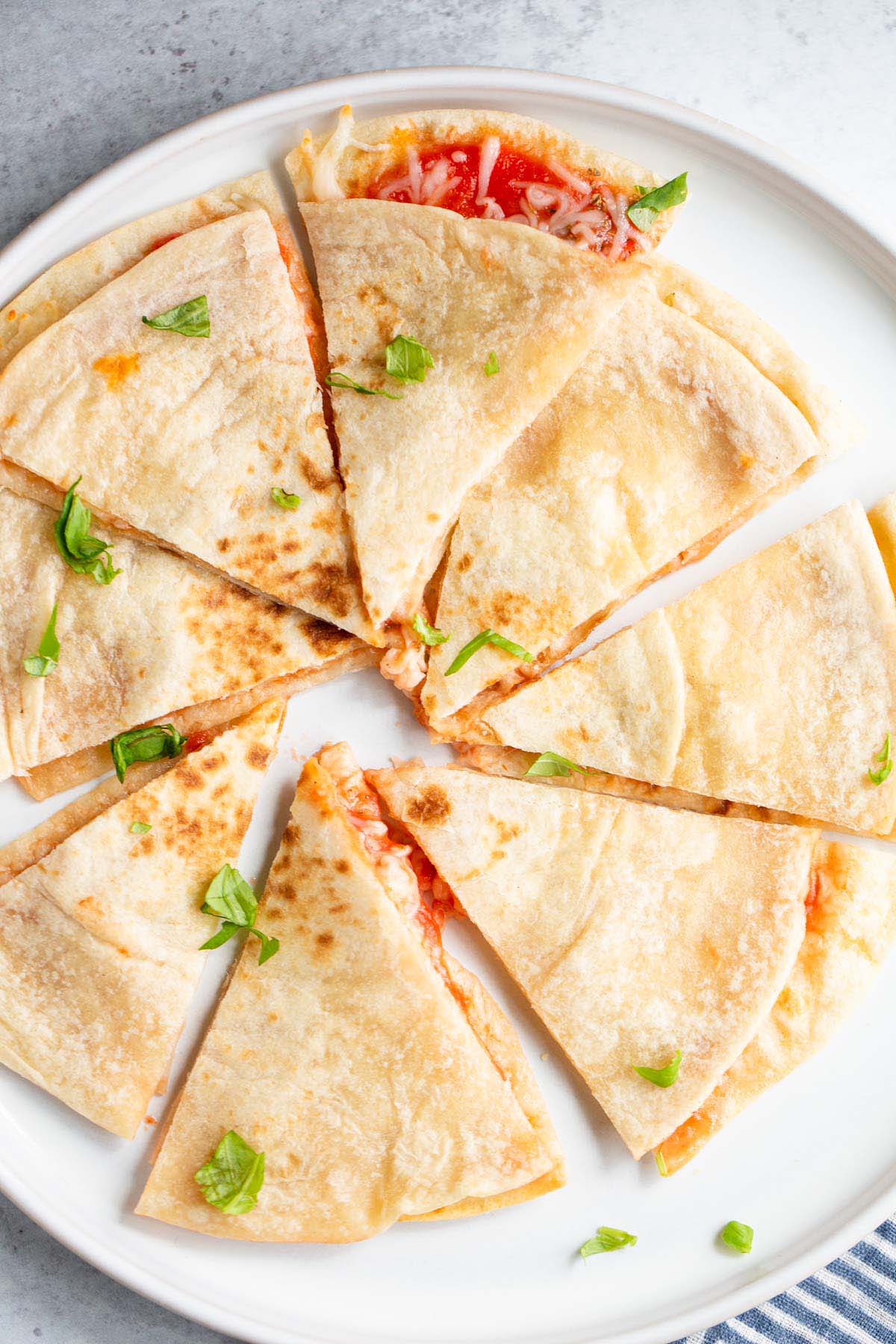 Air fryer pizza quesadilla on a white plate topped with chopped basil leaves.