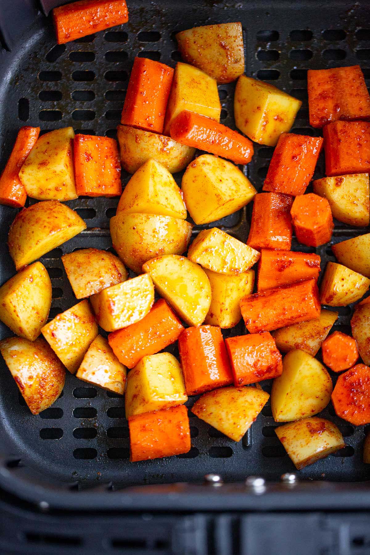 Uncooked potatoes and carrots in air fryer basket.