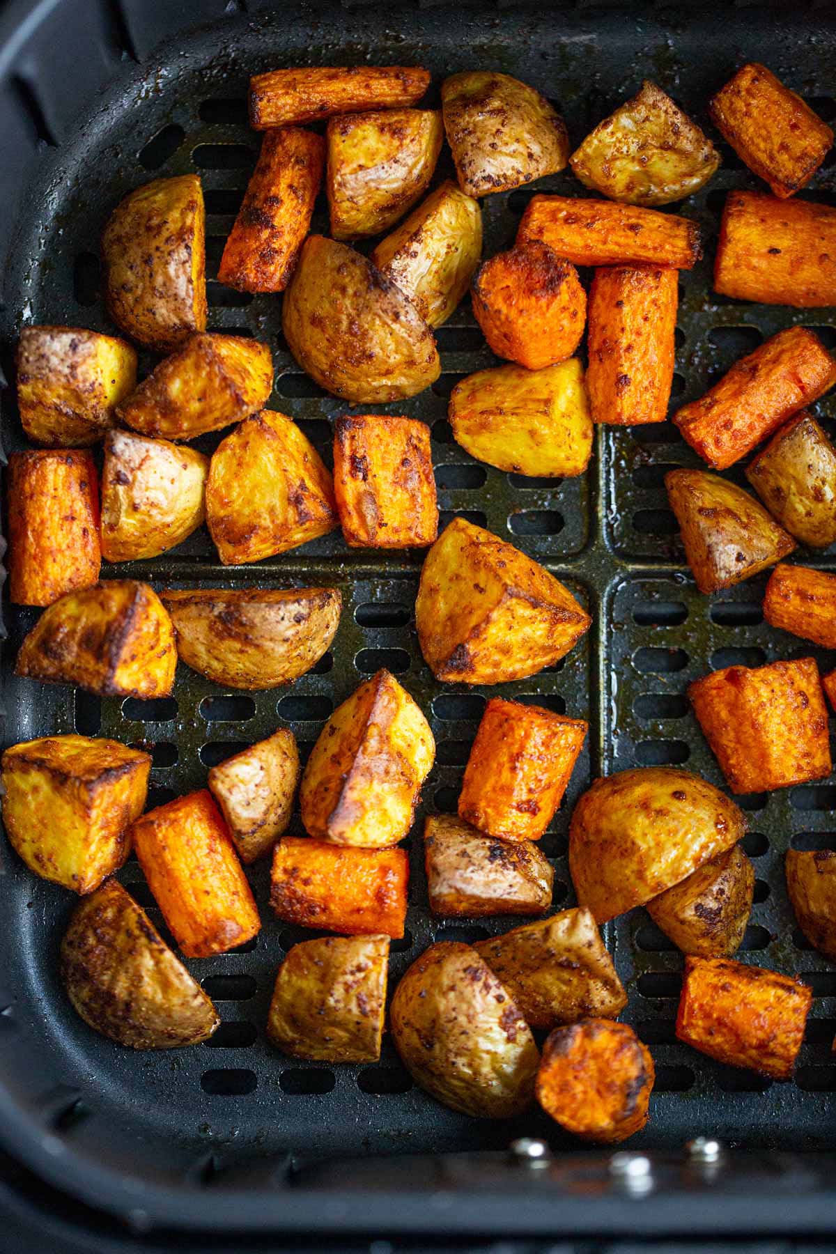 Roasted potatoes and carrots in air fryer basket.