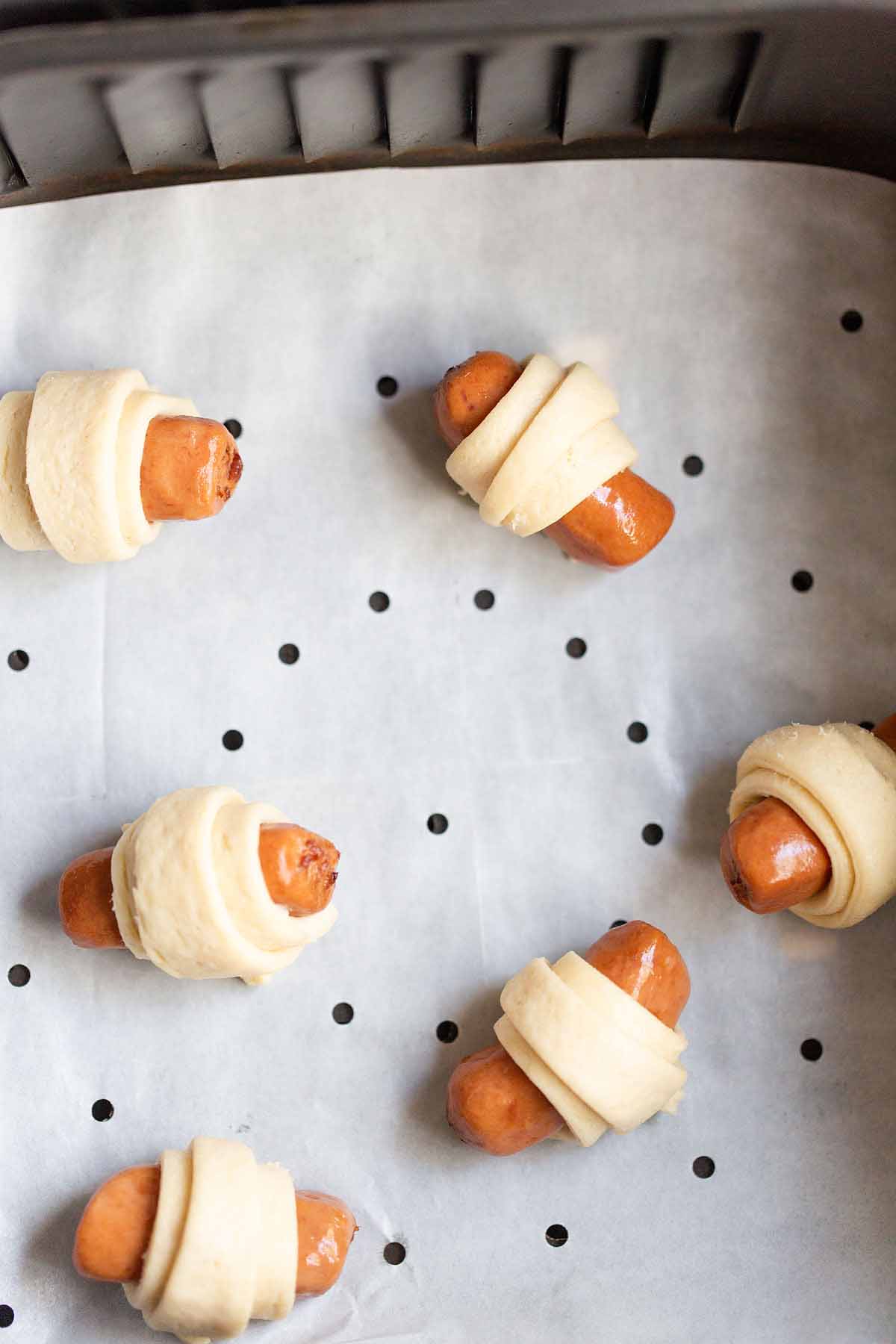 Uncooked pigs in a blanket in air fryer basket.