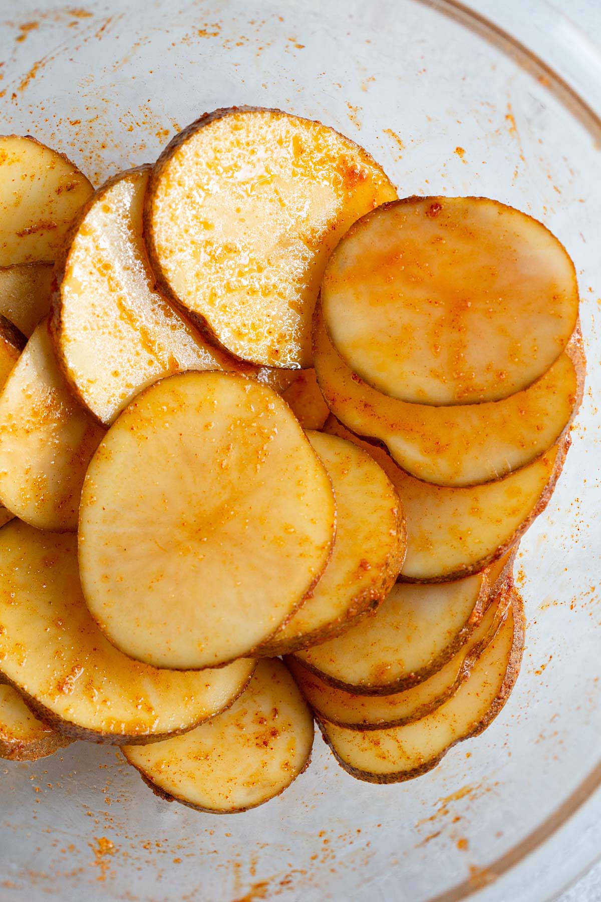 Potato slices in a bowl tossed with seasonings