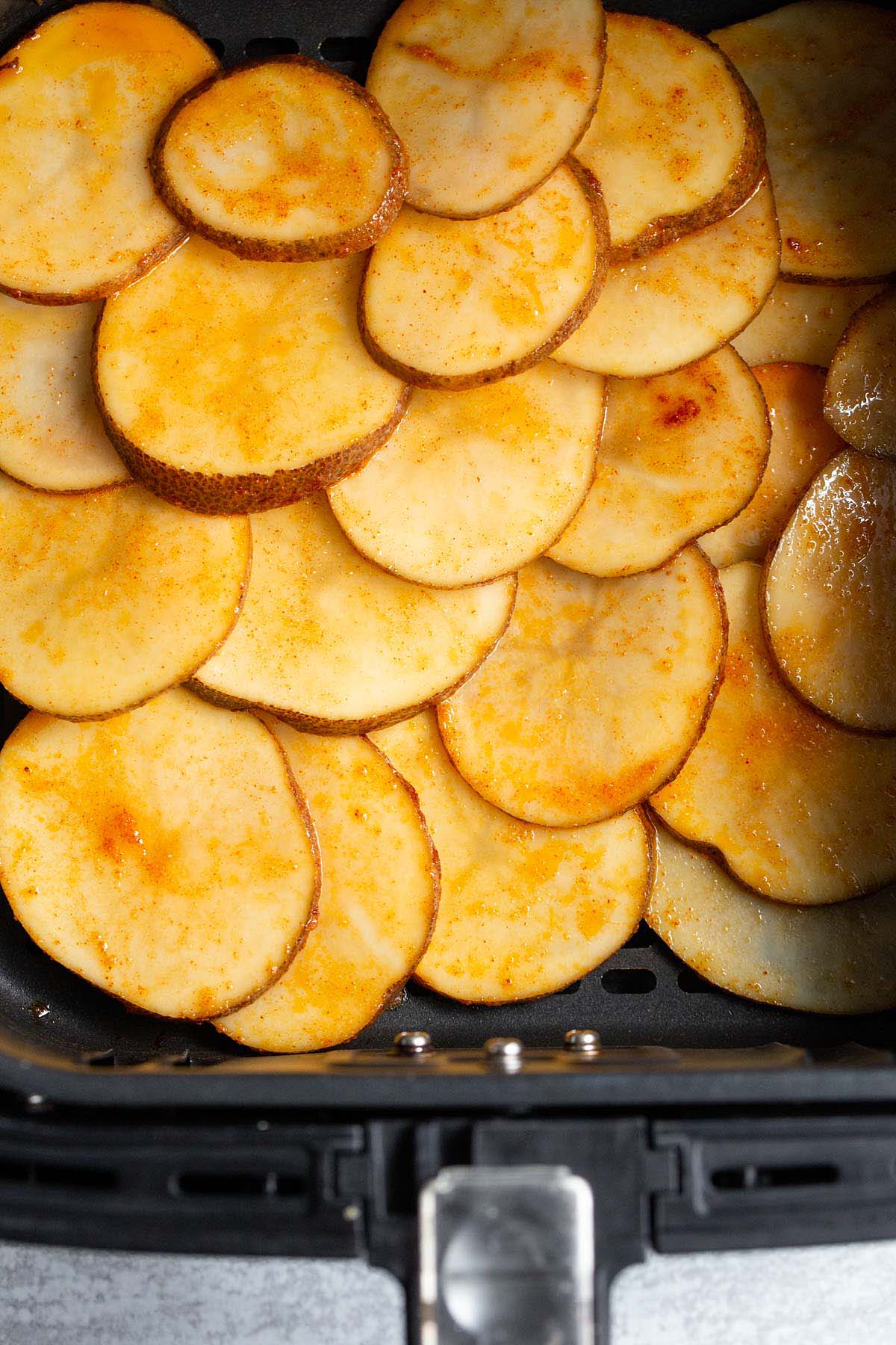 Uncooked potato slices in air fryer basket