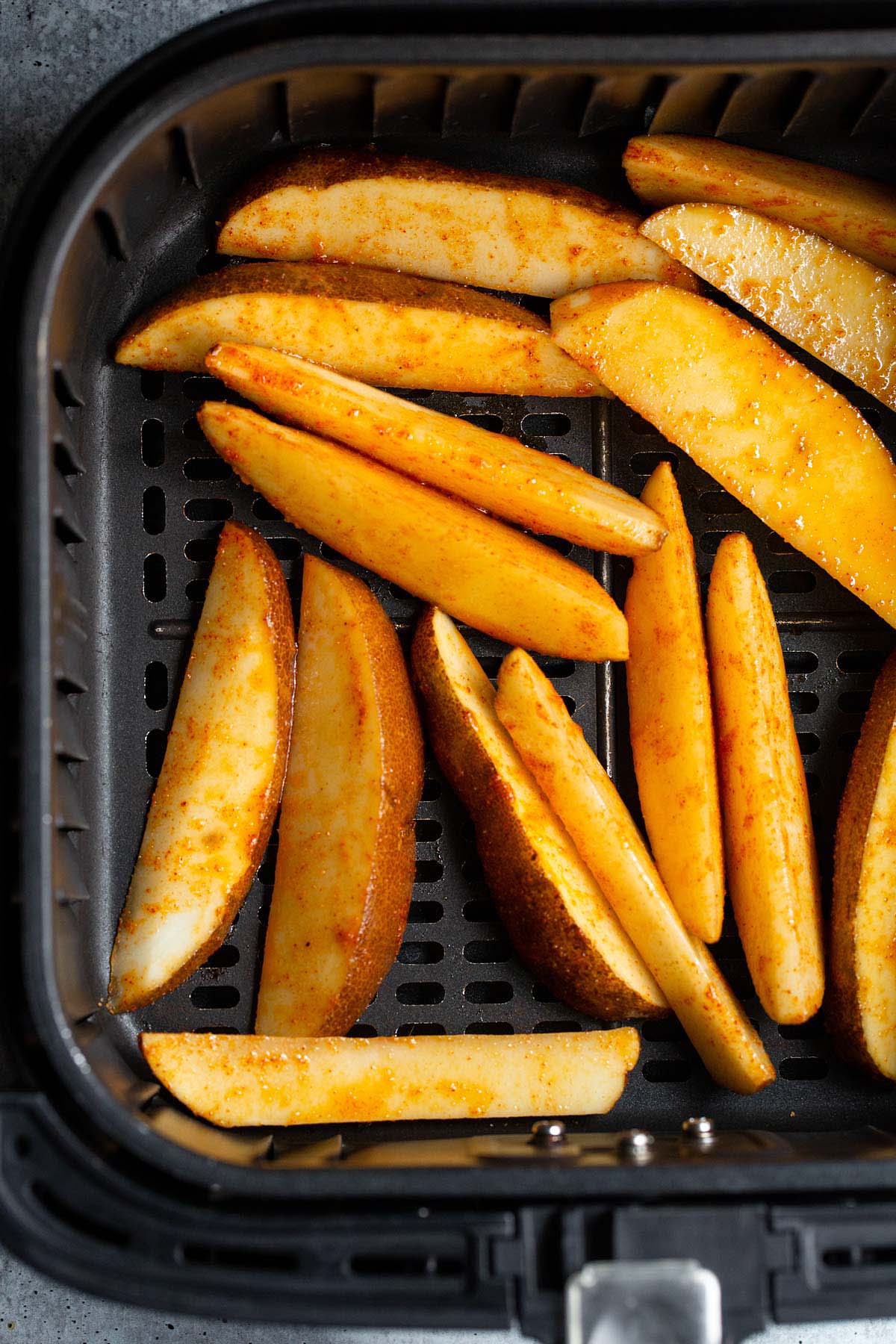 Uncooked potato wedges in air fryer basket