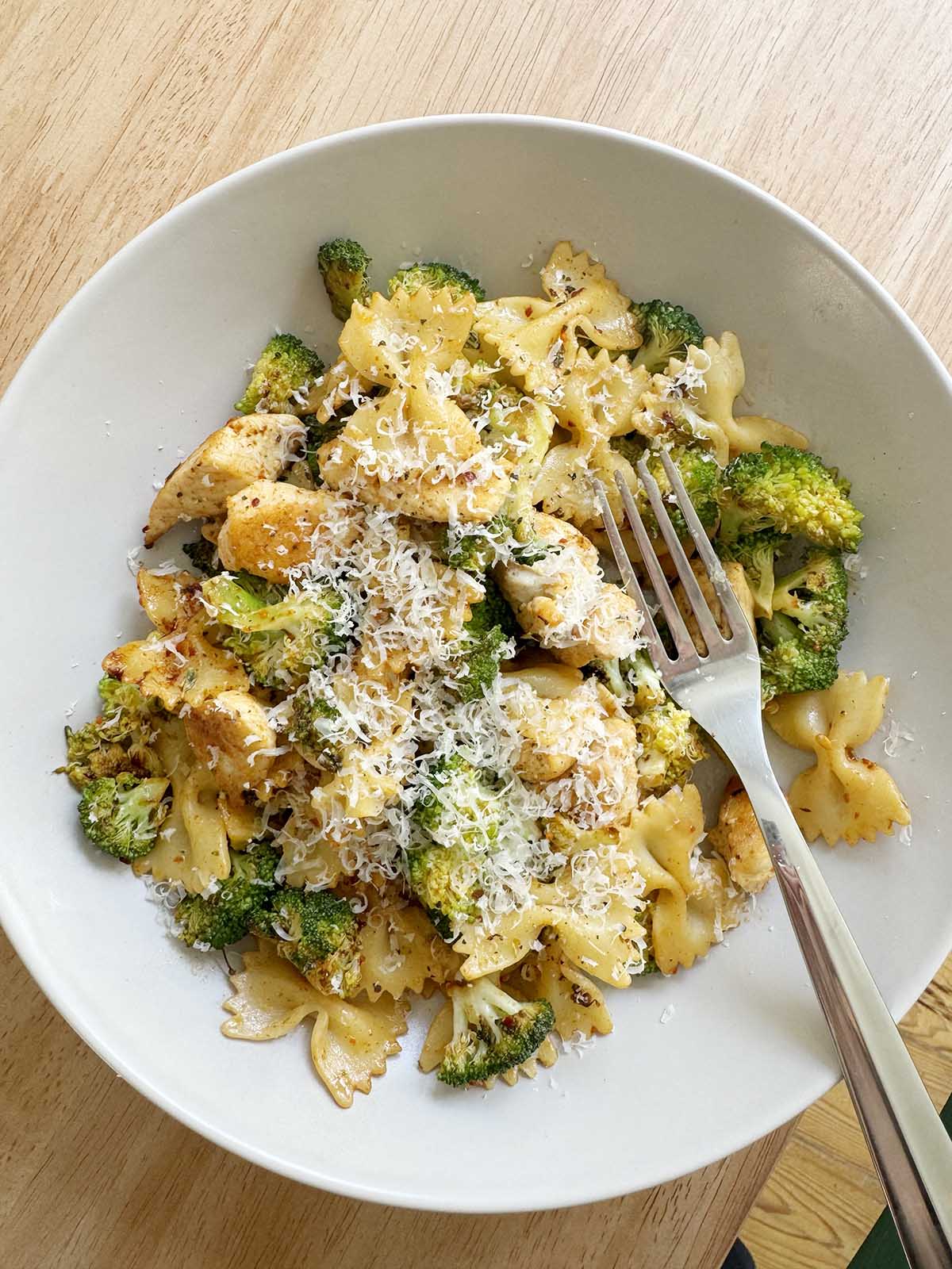 Chicken broccoli pasta in a bowl topped with parmesan cheese.