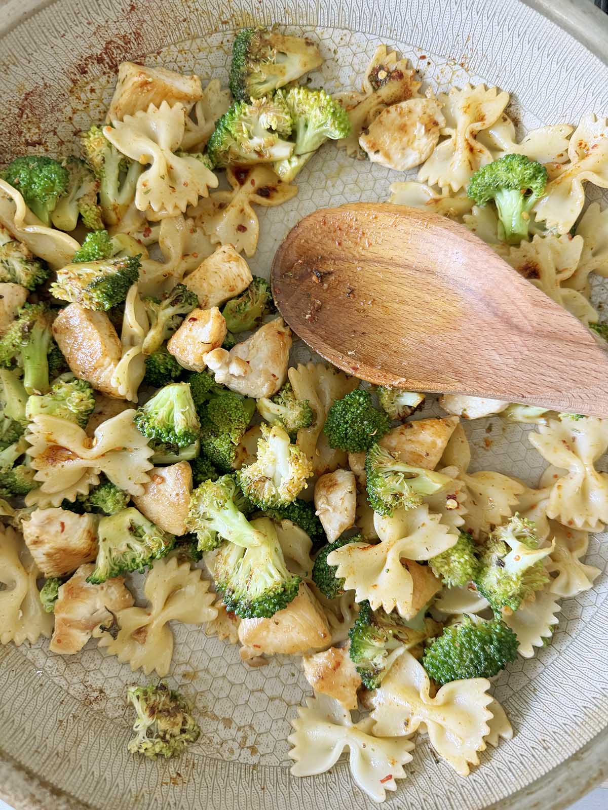 Stirring chicken broccoli pasta with a wooden spoon