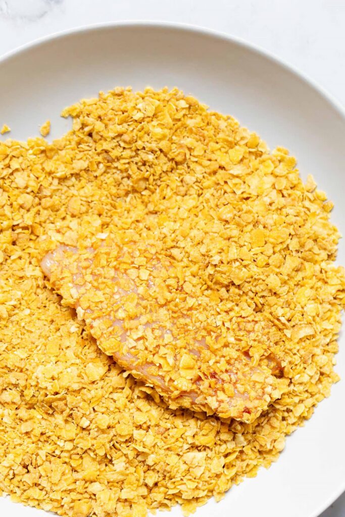 Chicken being crusted with crushed cornflakes