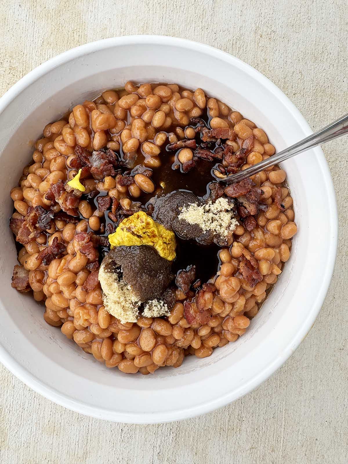Adding all ingredients for baked beans to a casserole dish