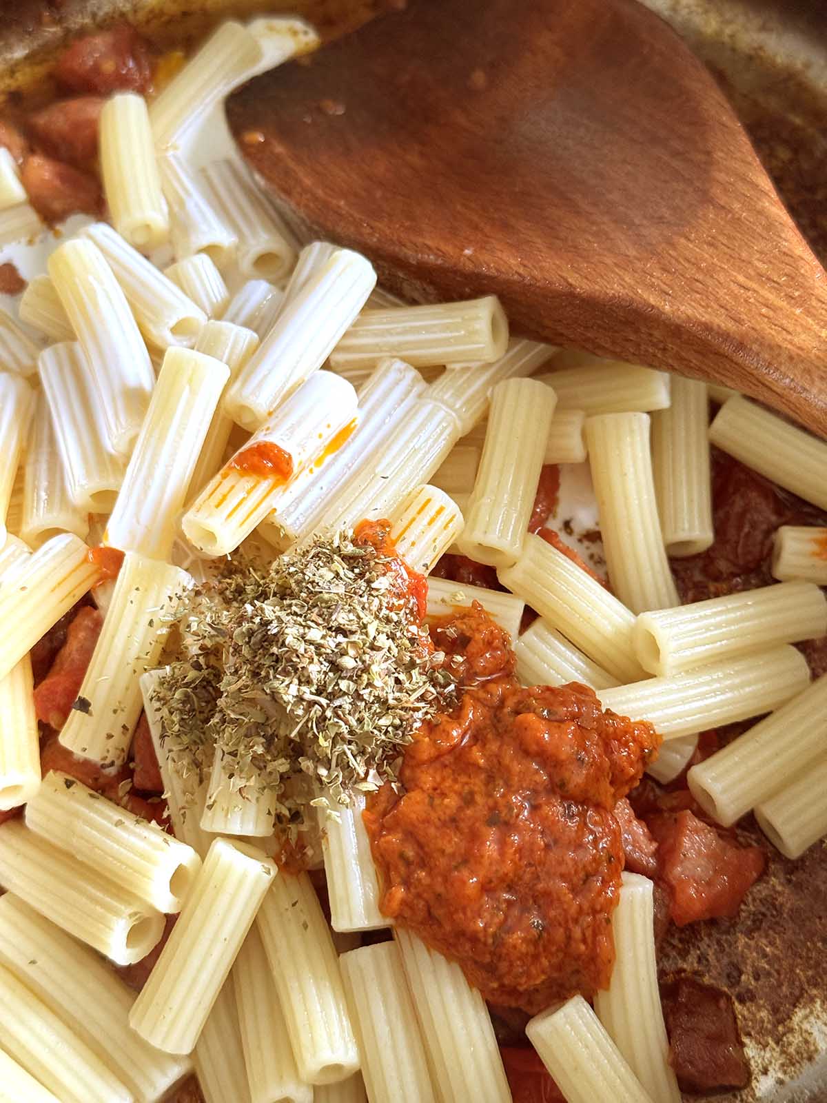 Adding cream, calabrian pesto, and oregano to pasta