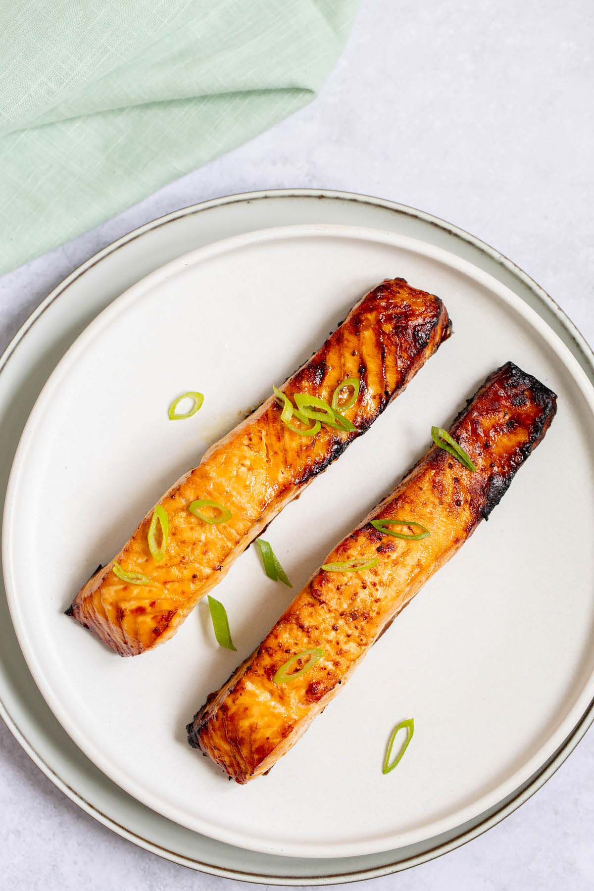 Two air fried salmon fillets on a plate with green onions