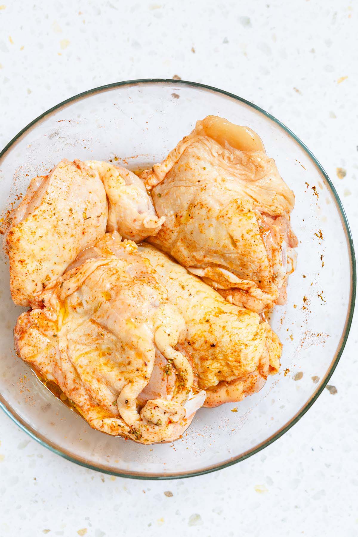 Uncooked chicken thighs marinating in a bowl